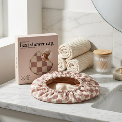 Pink and white checkered flexi shower cap on a marble surface with packaging and towels in the background.