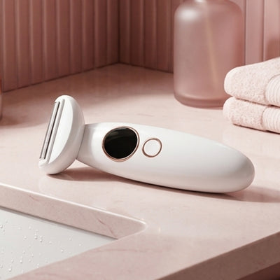 White electric razor on a bathroom counter with towels and bottles in the background